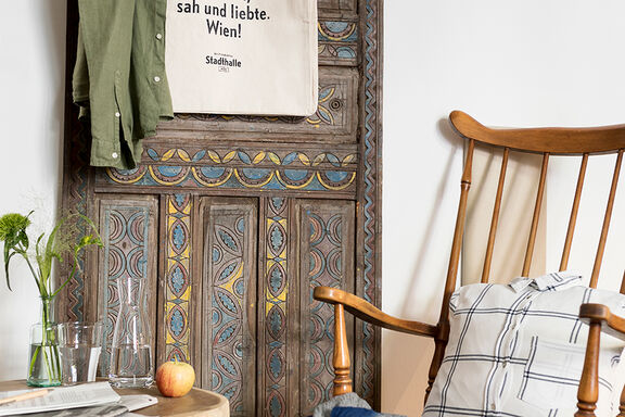 A wooden rocking chair stands next to a wooden cabinet that is decorated with bright colors and different patterns