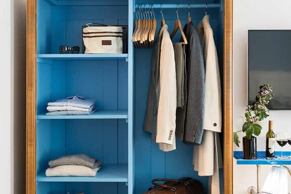 Several jackets are hanging in a blue wardrobe and several shirts are in one compartment in the same closet