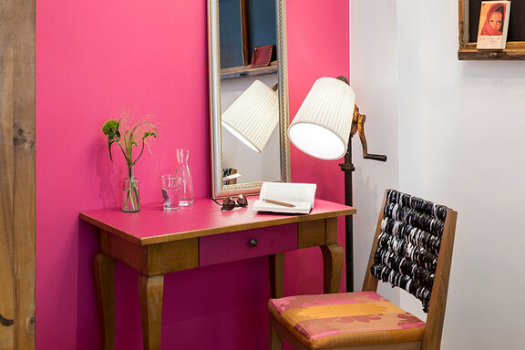 Ein Schreibtisch in rustikaler Holzoptik mit pinken Elementen steht vor einer pink angemalten Wand