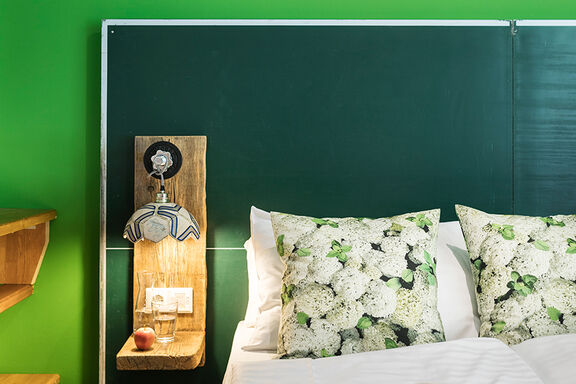 Photo of a bed in the boutique hotel Stadthalle with flower pillows and green walls