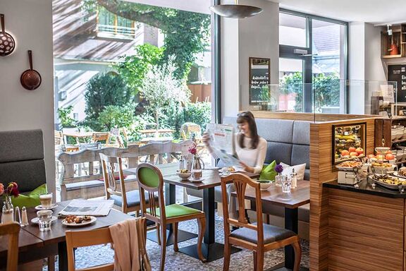 Frau sitzt am Frühstückstisch und liest eine Zeitung während sie einen Kaffee trinkt. / © Tina Herzl