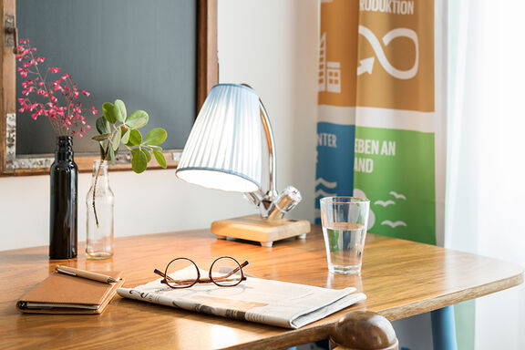 Reading glasses lie on a newspaper, which in turn lie on a table next to a reading lamp