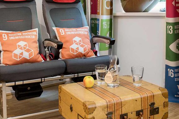 An apple, a jug and a glass of water stand on a side table in a suitcase design next to a sofa made of modern armchairs
