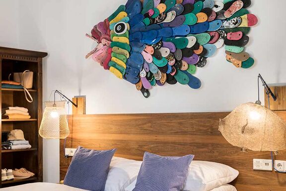 Ein großer bunter Fisch aus verschiedenen Recycle-Teilen hängt als Dekoration an der Wand