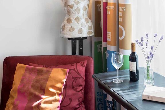 Foto von einer Flasche Rotwein und einem Rotweinglas auf einer grauen Kommode neben einem roten Lehnsessel