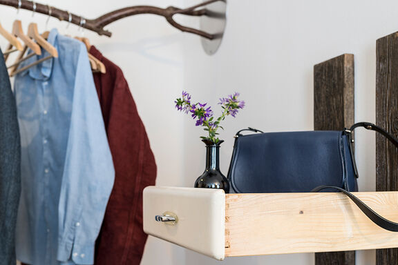 Eine blaue Handtasche steht neben einer schwarzen Vase in einer Schublade aus Naturholz